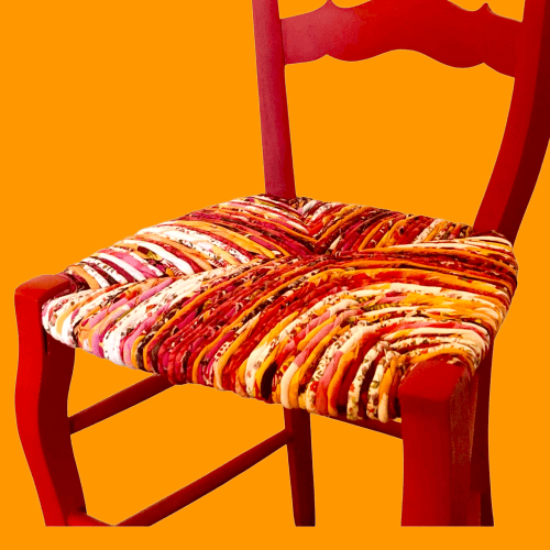 Chaise paillée ancienne revêtue d'un paillage dans les tons rouges, roses, prune, orange, écru, rose. Vue assise 2