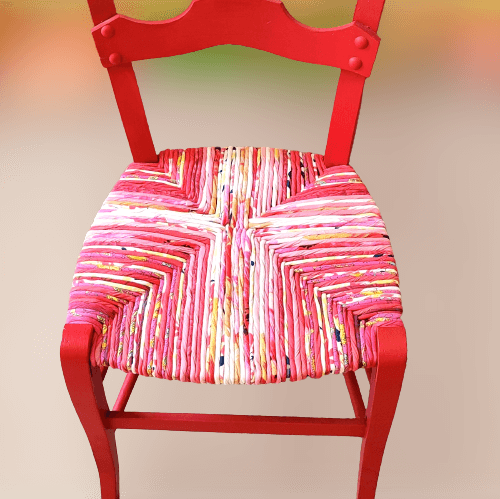 Chaise paillée ancienne revêtue d'un paillage dans les tons rouges, roses, écru avec une pointe de vert. Assise